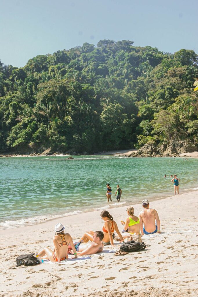 People enjoying a sunny day on a Costa Rican beach surrounded by tropical forest.