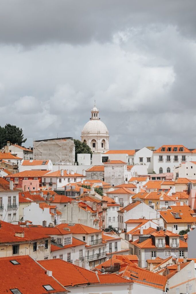 Panoramic view of Lisbon's iconic terracotta rooftops and historic architecture under a cloudy sky.