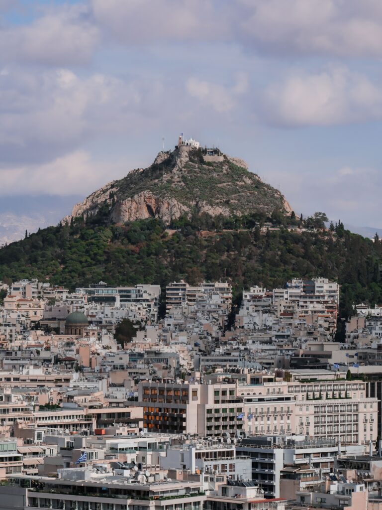 Aerial view of Mount Lycabettus overlooking Athens cityscape under a cloudy sky.